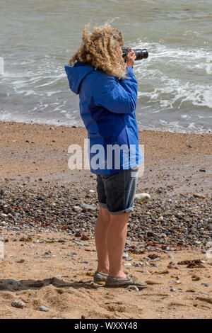Eine junge Frau Frauen stehen auf einem Strand mit einer SLR-Kamera die raue stürmische Winter Meer Foto Stockfoto