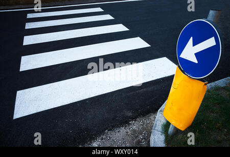 Ein blaues Schild mit einem weißen Pfeil zeigt Streifen für einen Fußgängerüberweg auf dem Asphalt einer Stadt Straße Stockfoto