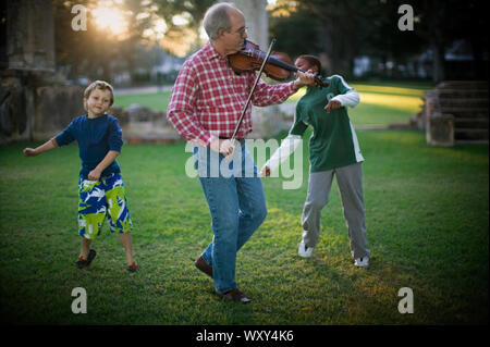 Älterer Mann spielt eine Violine zu zwei Jungen in den Hinterhof. Stockfoto
