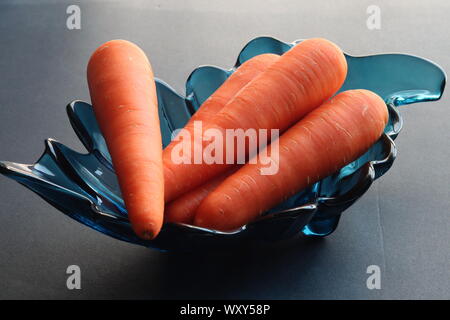 Bündel von Karotten in dekorativen Türkis blaues Glas Schüssel gegen Schwarz/grauer Hintergrund Stockfoto