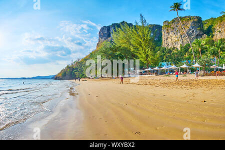 AO NANG, Thailand - 25 april 2019: Der lange tideline des Centara Grand Beach mit Sonnenschirmen, tropischem Grün und hohen Felsen auf der Rückseite Stockfoto