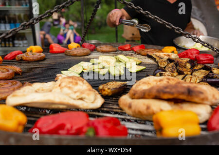 Ein großer runder Grill auf die Kohlen in der Farbe vom Grill Gemüse und frischem Fleisch Wurst gekocht werden. Essen und Ausrüstung für das Kochen zu einem Essen festiv Stockfoto