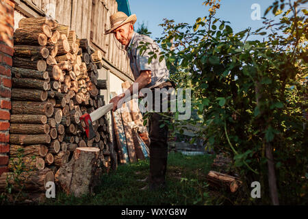 Arbeiten mit Axt. Älterer mann Zerkleinern von Brennholz mit einer Axt in der Landschaft Hof. Stockfoto