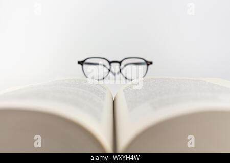 Close-up ein aufgeschlagenes Buch mit Brille auf weißem Hintergrund Stockfoto