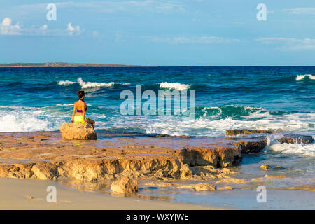 Frau im Bikini auf einem Stein saß, mit Meerblick Playa de Llevant, Formentera, Balearen, Spanien Stockfoto