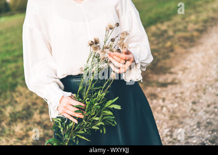 Junge Frau in einem Feld hält einen Zweig der flauschigen Herbst Löwenzahn in Ihren Händen Stockfoto