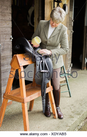 Eine Frau, Reinigung und Vorbereitung Tack und Sattel im Hof des einen Reitstall.