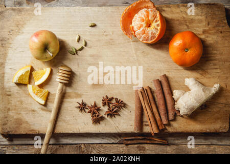 Flatlay con ingredientes para cocinar vino caliente. Manzana, mandarina, canela, estrellas de anís, el cardamomo y el jengibre en la tabla de cortar de madera Foto de stock
