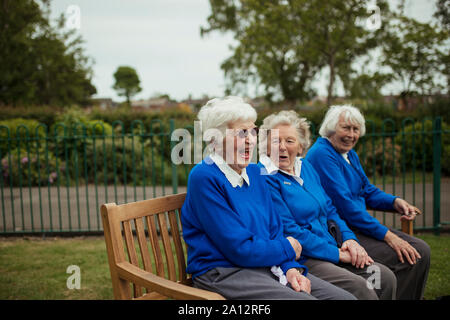 Un primer plano de las mujeres ancianas sentadas en un banco en un bowling green riendo.