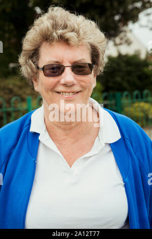 Un retrato de una mujer sonriente senior en bowling green. Ella lleva gafas de sol.
