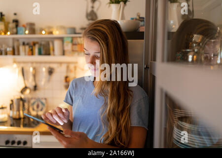 Mujer joven en cocina en casa utilizando tablet