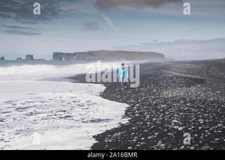 Mujer joven caminar descalzo en una playa de lava en Islandia