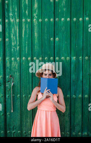 Retrato de mujer joven de pie delante de la puerta de madera verde con un libro en verano Foto de stock