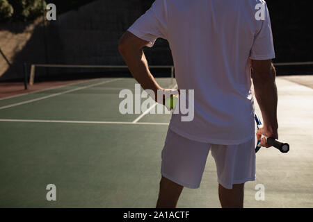 El deporte del tenis. Hombre jugando al tenis al aire libre. Retrato de  joven atractivo en camiseta blanca con la raqueta y la bola en el fondo del  cielo. Un estilo de