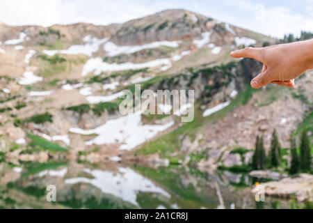 Albion Basin, Utah verano con acercamiento de señalar con el dedo en el reflejo del agua en el lago Cecret en montañas Wasatch con rocas, nieve y de color verde Foto de stock