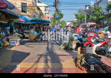 Un hombre duerme profundamente en un sendero fuera Pak Klong Talaat (mercado) en Bangkok, Tailandia, a pesar de la actividad frenética de él Foto de stock