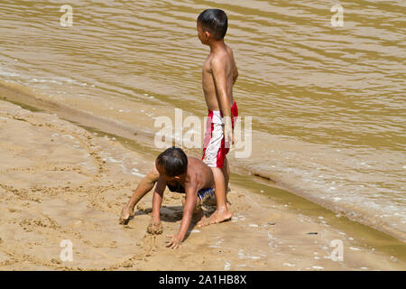 Unknown niños jugando con la arena y el agua por el río Belaga en Sarawak, Malasia Foto de stock