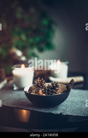 Encendido de velas y decoración natural de conos, tuercas en negro recipiente sobre la servilleta de tela gris en el cuadro negro. Ambiente acogedor en casa. Familias Hygge SL