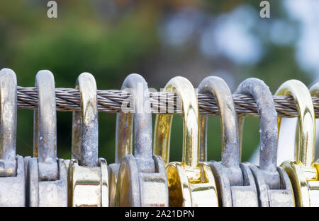 Candados de oro en forma de corazón colgado en una cerca de alambre de acero shot y macro. Foto de stock
