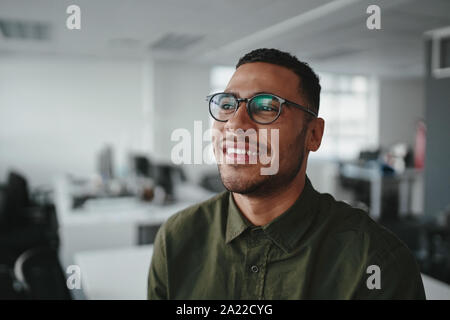 Retrato de un meditado sonriente joven hombre de negocios moderno en la oficina mirando lejos Foto de stock