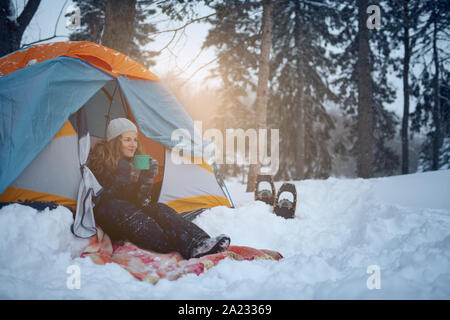 Ajuste chica rubia milenaria campamento con una carpa en un parque de nieve filles canadiense durante una excursión con raquetas de nieve Foto de stock
