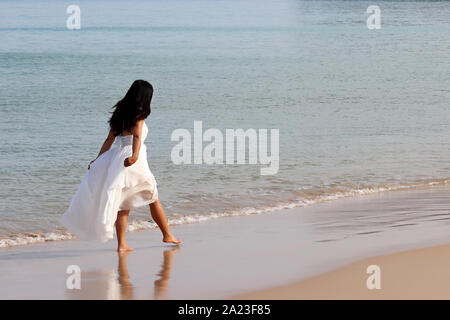 Mujer en un vestido blanco caminando en una playa en el fondo del mar por la mañana, feliz viajero. Luna de miel, vacaciones y viajes, romance y libertad