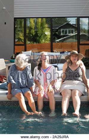 Feliz, despreocupado de las mujeres mayores amigos hablando y sumergir las piernas en la soleada, piscina de verano