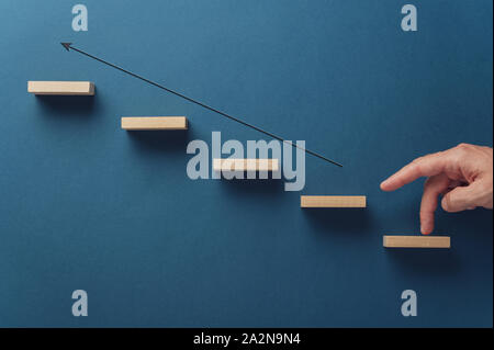 Los dedos masculinos caminando a lo largo de la flecha que señala hacia arriba por la escalera de espigas de madera en una imagen conceptual del crecimiento empresarial. Sobre azul marino backgrou