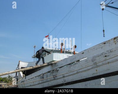 Yakarta, Indonesia - Julio 13, 2009: un hombre sube a un barco de madera sobre una viga de madera en la parte delantera de un barco de madera en color blanco, verde y rojo Foto de stock