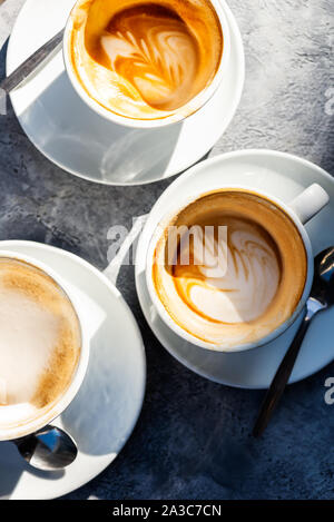 Tres tazas de vacío plana blanca, un café en la cafetería, bonito día soleado, sombras sobre la mesa
