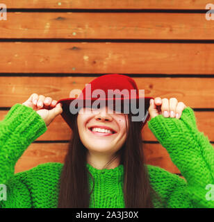Atractivo femenino riéndose de pie contra la pared de madera fondo con espacio de copia, bastante casualmente vestida hipster mujer mirando lejos sonriendo un Foto de stock