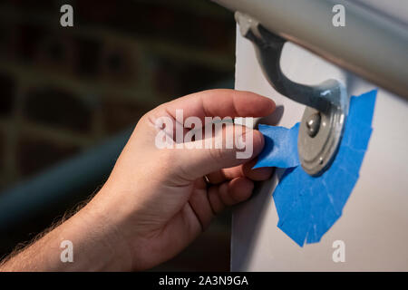 Mano tapando el borde de la barandilla con el pintor azul cinta para preparar una capa de pintura fresca Foto de stock