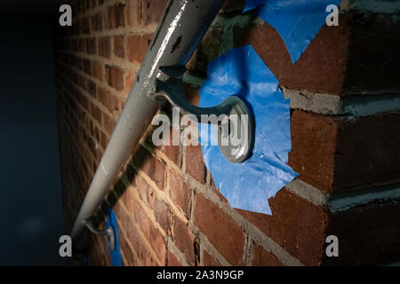 Barandilla metálica en pared de ladrillo con cinta azul de pintor, preparada para una nueva capa de pintura Foto de stock