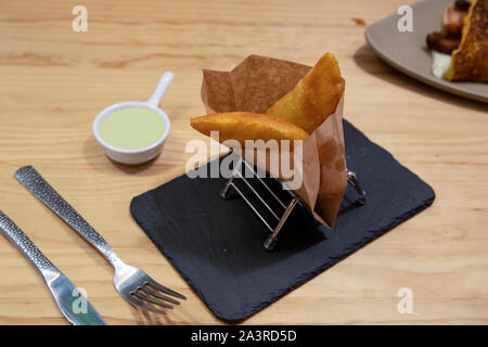 Deliciosas empanadas típicas de la comida latina envuelto en papel sobre placa de piedra sobre fondo de madera Foto de stock
