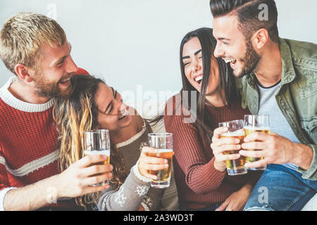 Grupo de Amigos felices animando con cerveza en casa - Jóvenes milenario divertirse bebiendo y riendo juntos sentados en el sofá Foto de stock