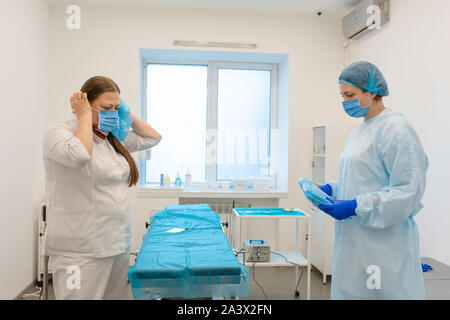 Una enfermera vestidos un cirujano en un traje estéril antes de la cirugía. Foto de stock
