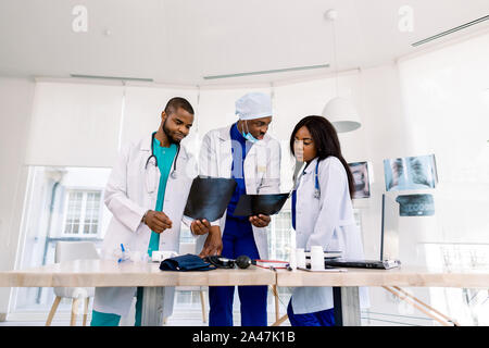 Salud: grupo de tres jóvenes doctores africanos, dos hombres y una mujer, discutir y mirando x-ray en una clínica u hospital. Foto de stock