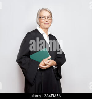 Mejor asesoramiento jurídico concepto: retrato de una amable sonrisa juez madura con libro de derecho en sede judicial vestido