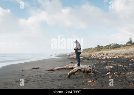 Hombre de pie en driftwood mirando el teléfono móvil en la playa.