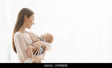 Mujer sosteniendo bebé recién nacido y mirando con amor y cuidado Foto de stock