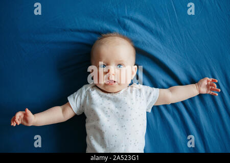 Retrato de cute adorable niña caucásica blanca sonriente joven con ojos azules 4 meses tumbado en la cama en la habitación mirando a la cámara. Vista anterior