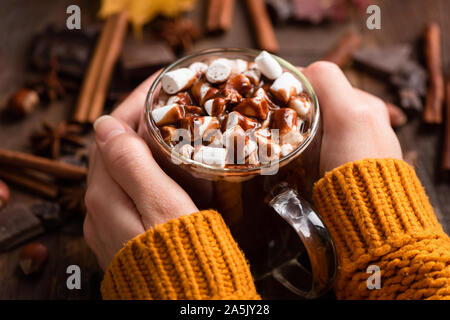 Taza de chocolate caliente con malvaviscos, canela y salsa de chocolate en manos femeninas. Visión más cercana. Comida cómoda para otoño e invierno