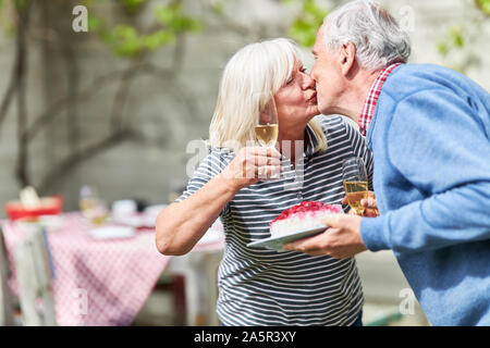 Pareja de ancianos besándose en una fiesta de cumpleaños o una fiesta en el jardín Foto de stock