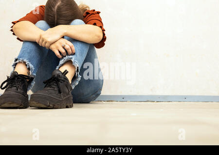Mujer joven grita y sentarse cerca de una pared vacía, triste triste y deprimida Chica sujetando su cabeza abajo Foto de stock