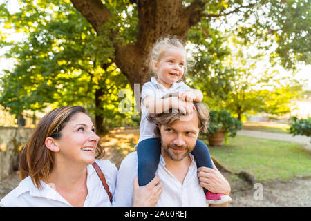 Familia feliz en un parque con el padre llevando sobre sus hombros una hija pequeña
