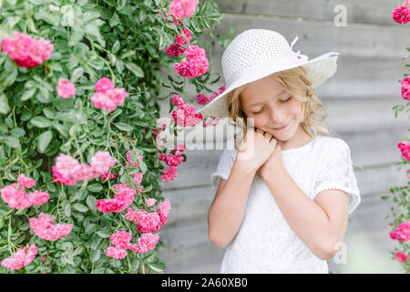 Retrato de niña sonriente con los ojos cerrados en el rosal