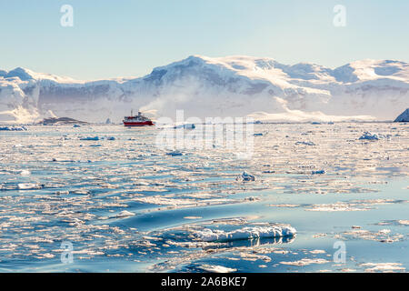 Rojo crucero Steamboat deriva afar entre los icebergs con enormes rocas y glaciar de fondo, Nechâo Bay, en la Antártida Foto de stock