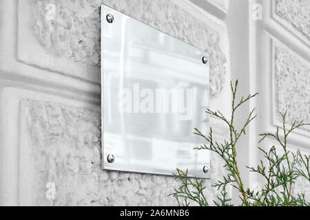 Letrero de vidrio plateado en blanco sobre pared con textura gris Foto de stock