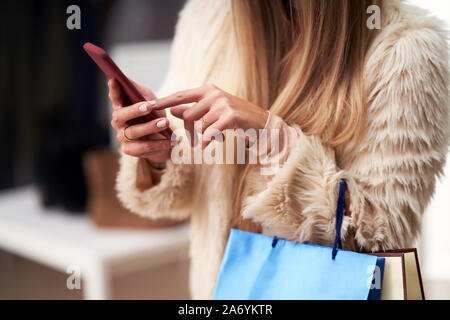 Las mujeres adultas compras para la ropa en la boutique en otoño y utilizando el smartphone