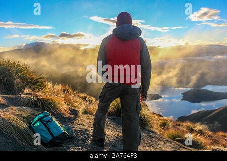 Hombre en ropa de lluvia mirando hacia las nubes en la cima de la montaña en NZ.